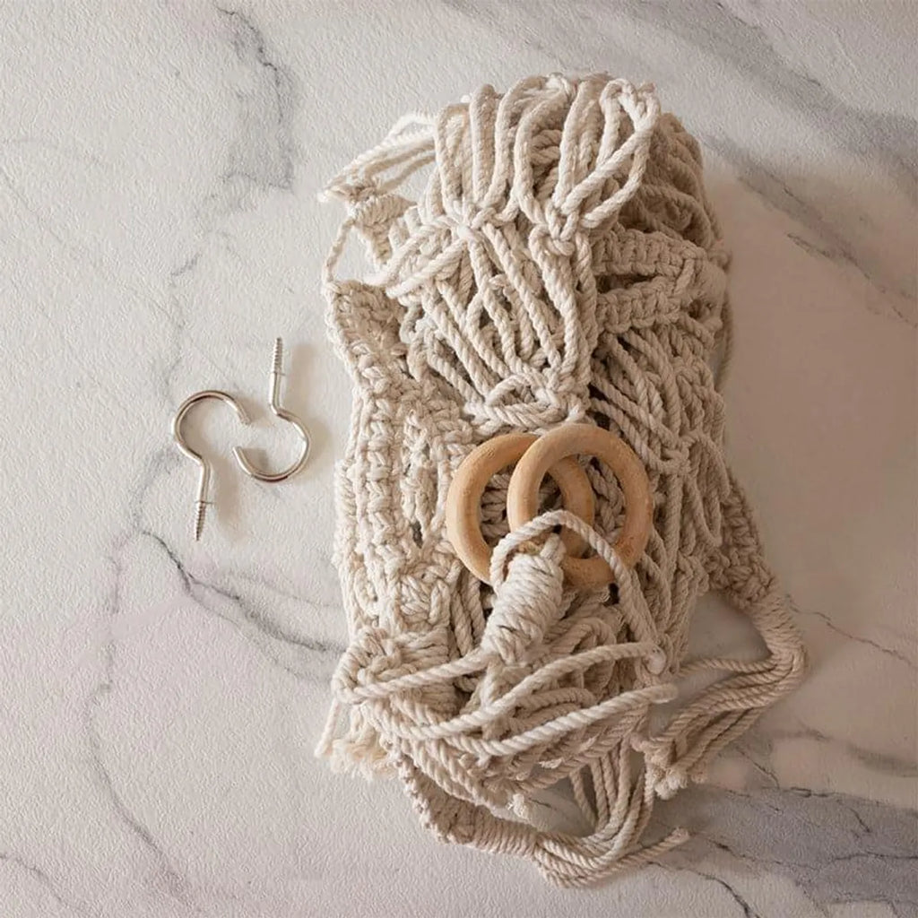 Soft white macrame toy hammock styled on wall